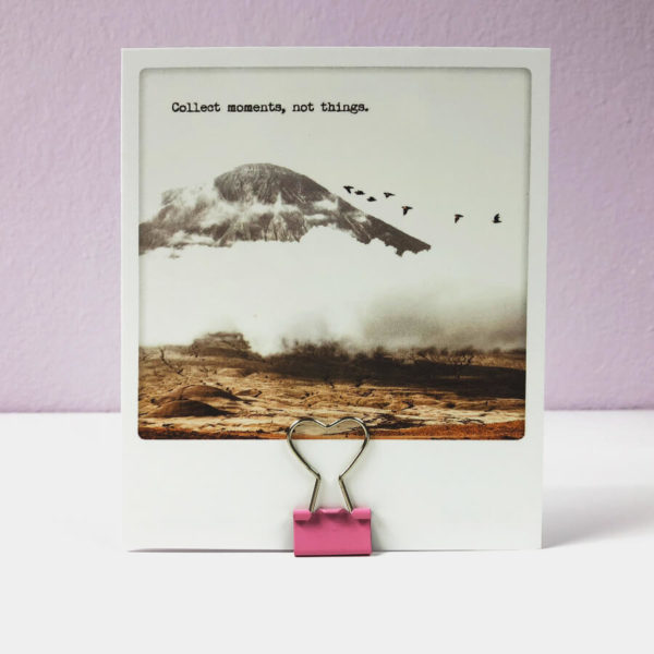 Eine rosane Papierklammer in Herzform die eine Postkarte mit der Aufschrift "Collect moments, not things" hält.
