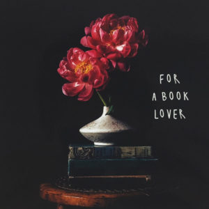 Nahaufnahme der Polaroid Karte mit Aufschrift "For a book lover" und einer Blumenvase, die auf einem Stapel Büchern steht.
