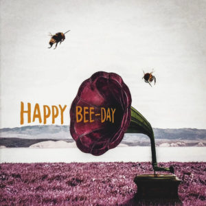 Nahaufnahme der Polaroid Karte mit Aufschrift "Happy Bee-Day" und zwei Bienen, die um ein Megaphone fliegen.
