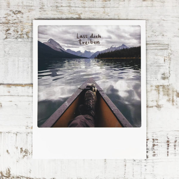 Polaroid Karte mit Aufschrift "Lass dich treiben" und Mann in einem Boot, der die Beine übereinander geschlagen hat.