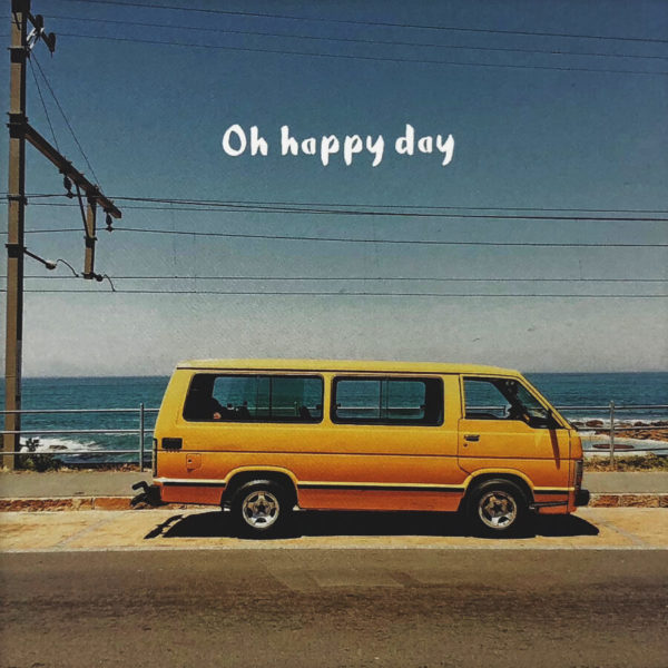 Nahaufnahme der Polaroid Karte mit Aufschrift "Oh happy day" und gelbem Kleinbus, der am Meer parkt.