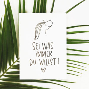 Postkarte mit Aufschrift "Sei was immer du willst!" mit Einhornkopf und Herz auf einem grünen Blatt.
