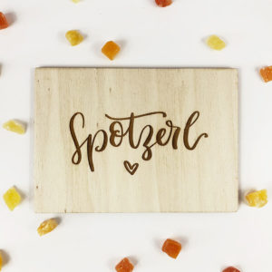 Holzpostkarte mit Aufschrift "Spotzerl" und kleinem Herz. Von oben fotografiert.