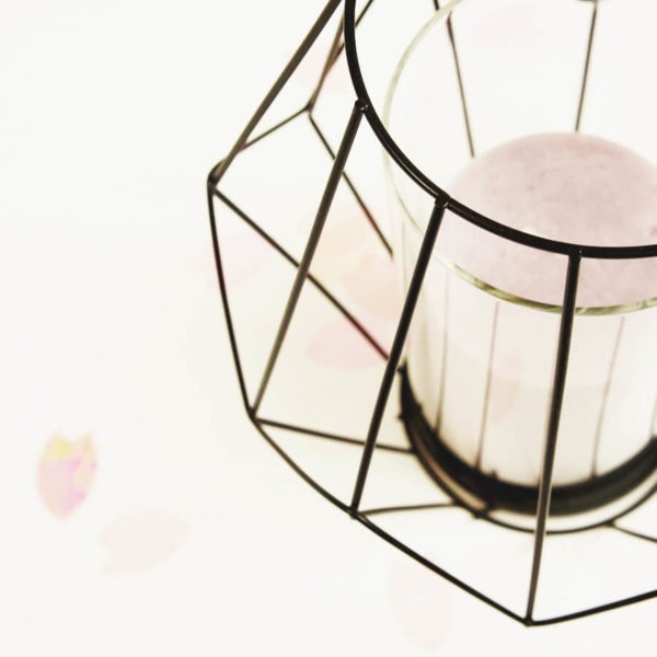 Schwarzes Teelicht aus Metall mit rosaner Kerze und Konfetti im Hintergrund.