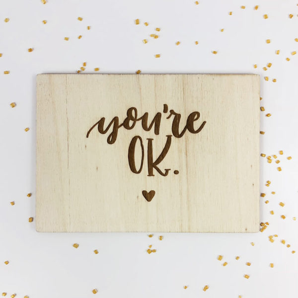 Holzpostkarte mit Aufschrift "You're OK" und kleinem Herz. Von oben fotografiert.